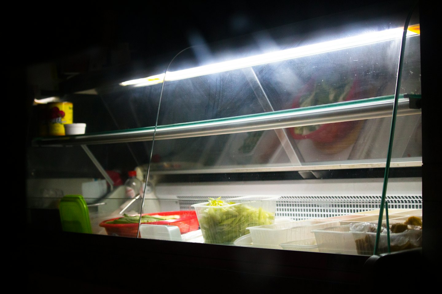 Fresh vegetables arranged in containers inside a food display case.
