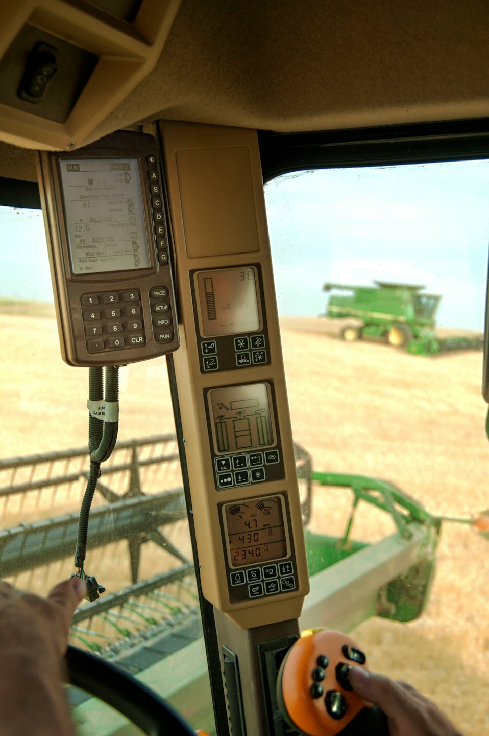 Hands operate a combine harvester joystick, looking at screens.