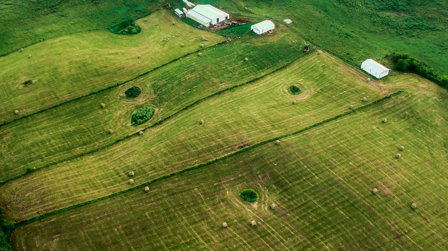 Aerial view of green farm fields with hay bales and trees.