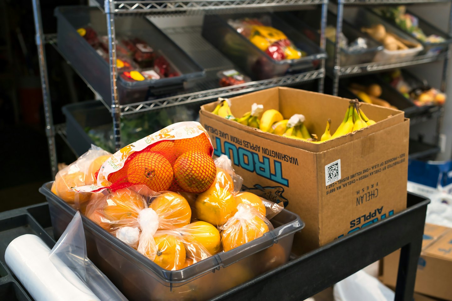 Oranges and bananas on a utility cart with a box of bananas.